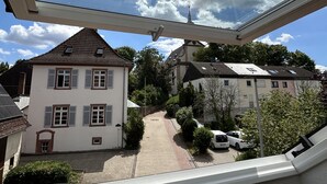 Une vue à travers un puits de lumière sur un quartier résidentiel avec des maisons, une allée pavée et des voitures garées.