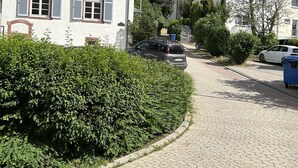 Une rue pavée menant à un bâtiment blanc doté de volets et à une église surmontée d’une flèche.