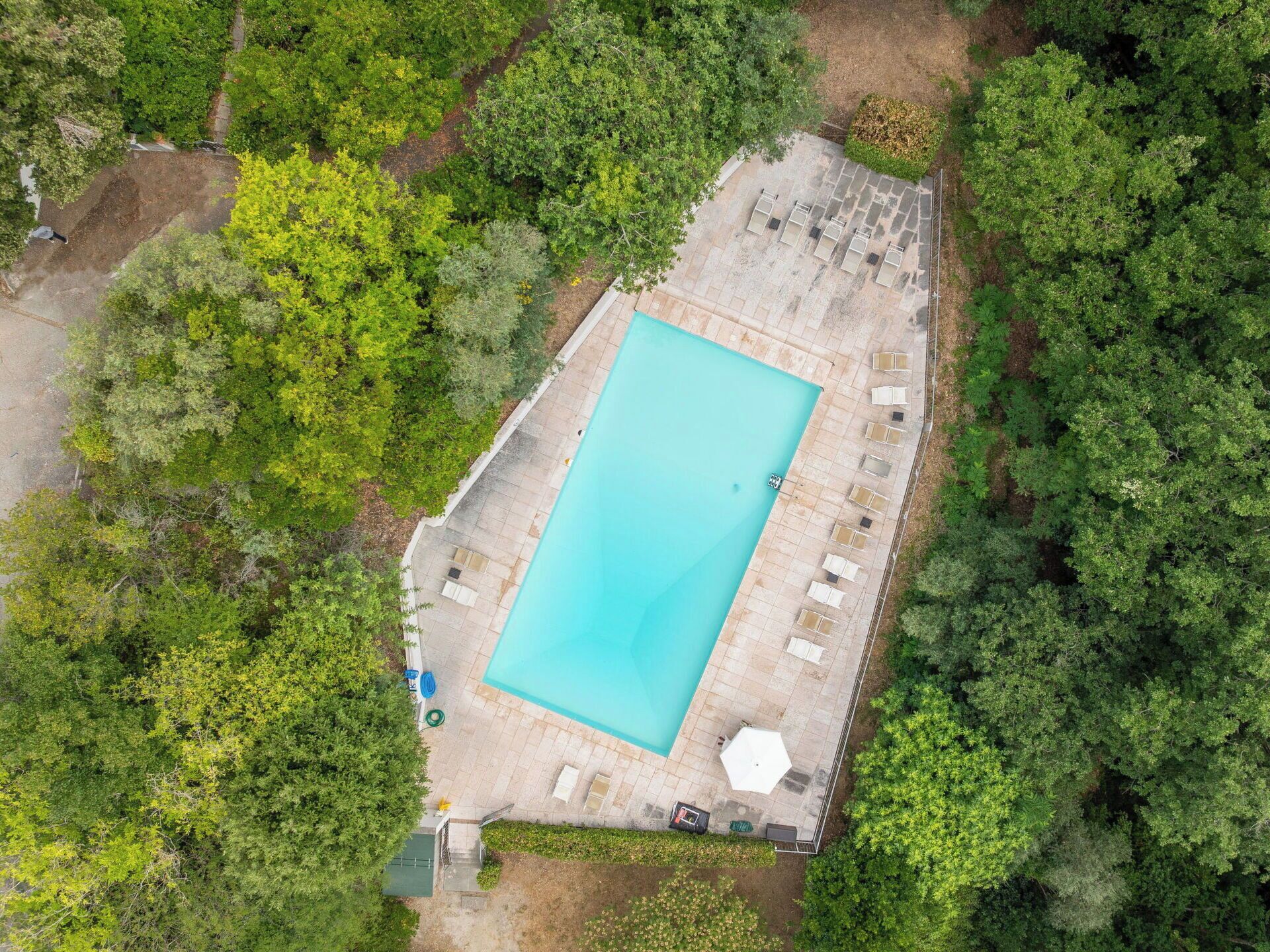 Une vue aérienne d’une piscine rectangulaire entourée d’une terrasse dallée, agrémentée de chaises longues et d’un petit espace jardin.