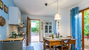 Et moderne køkken med spiseplads, med et træbord og stole, en hængende lampe og udsigt til haven gennem den åbne dør.