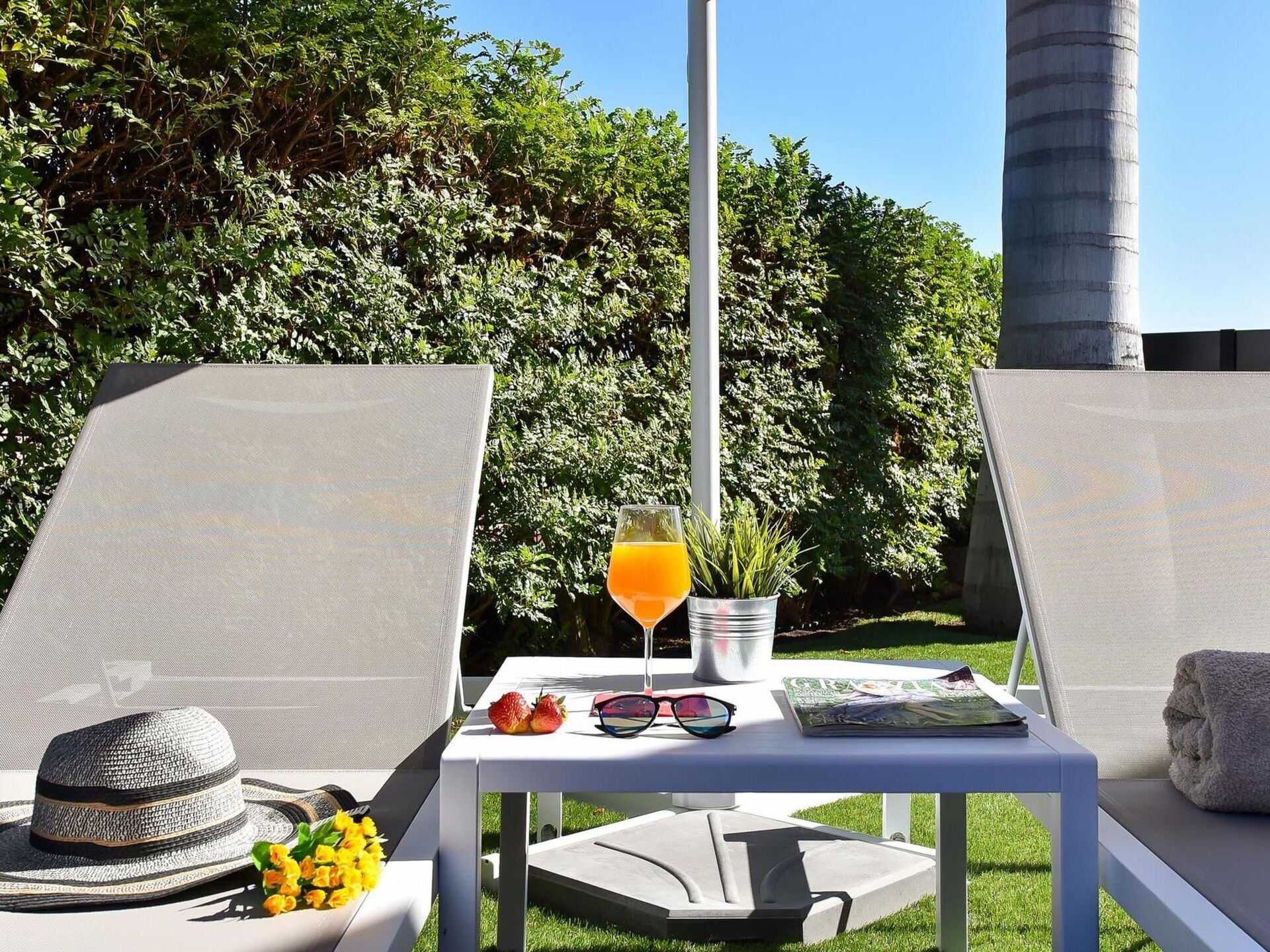 Un espace extérieur ensoleillé, aménagé avec des fauteuils confortables, une table avec une boisson, des lunettes de soleil et un chapeau.