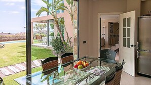 Une cuisine moderne dotée d’un réfrigérateur en acier inoxydable, d’une table à manger en verre avec des chaises, et offrant une vue sur le jardin arrière.