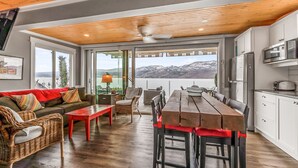 Un salon moderne avec un plafond en bois, un canapé, une table à manger et un coin cuisine offrant une vue sur les montagnes.