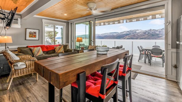 Un salon moderne avec un plafond en bois, de grandes fenêtres, une table à manger et une vue sur un lac et des montagnes.