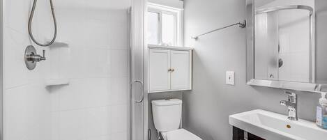 Uma casa de banho moderna com chuveiro, sanita e lavatório.
