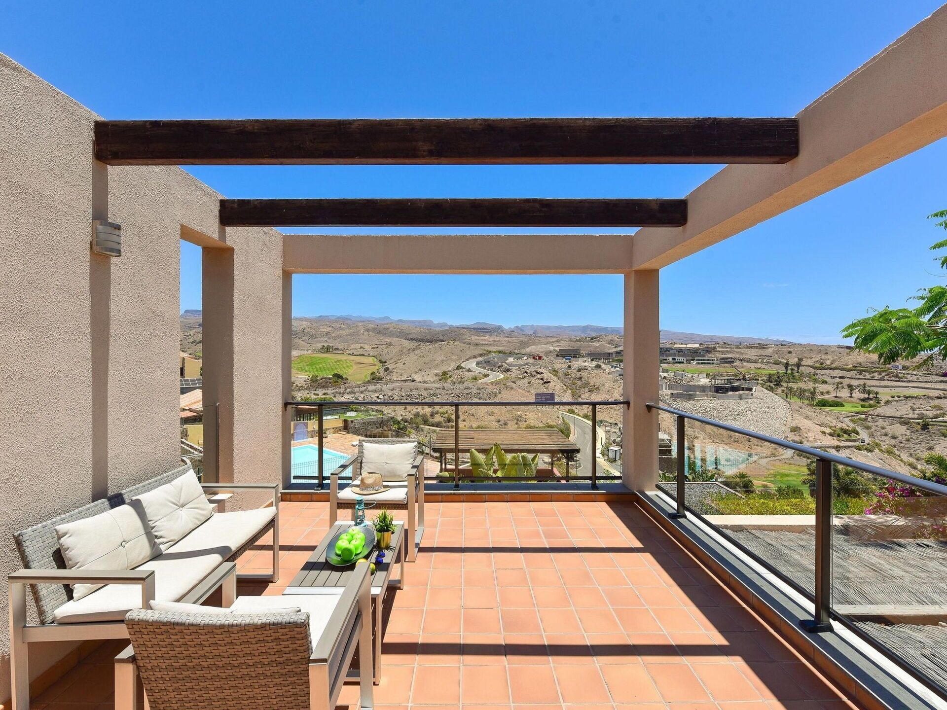 En balkon med udsigt over et kuperet landskab, udendørs møbler og en pool.