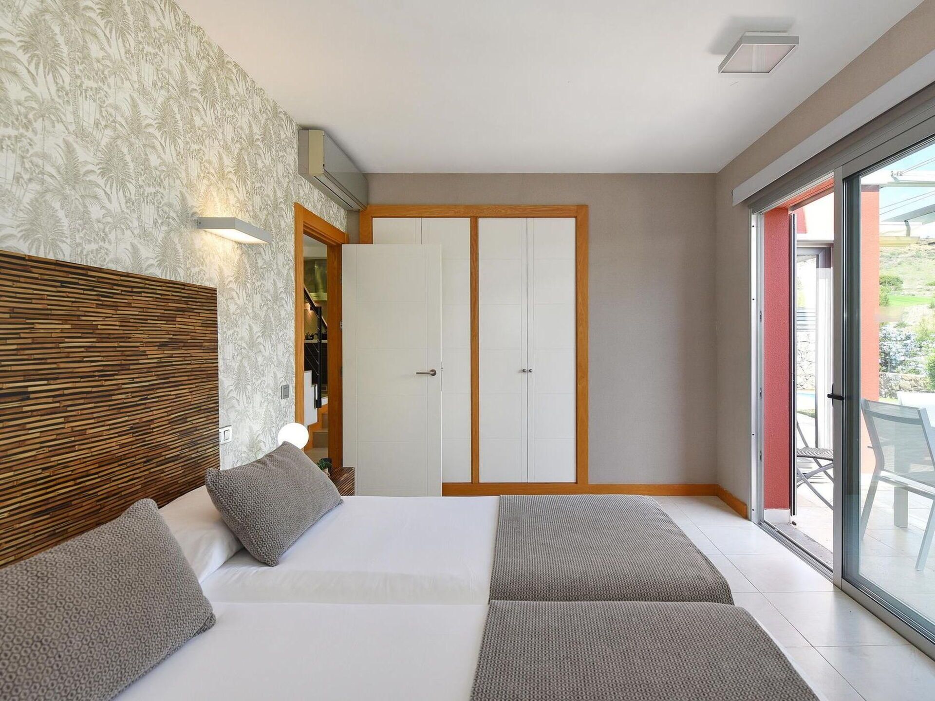 Un dormitorio moderno con una cama grande, un armario y un ventanal corredera que da a un balcón.