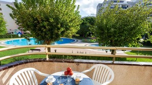 A terrace with a round table and white chairs, overlooking a swimming pool and greenery. - Nice apartment for 4 people with pool, WIFI, TV and patio (Salou)