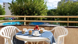 A balcony with a table set for breakfast, overlooking a swimming pool and trees. - Nice apartment for 4 people with pool, WIFI, TV and patio (Salou)