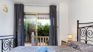 A bedroom with a bed, a nightstand, a lamp, a balcony with curtains, and a view of greenery outside. - Beautiful apartment for 4 people with pool, WIFI, A/C, TV and patio (Salou)