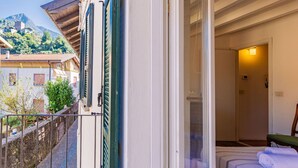 Une chambre d’hôtel avec un balcon, un lit recouvert d’une couvre-lit à rayures bleues, et une vue sur les bâtiments et les montagnes environnants.