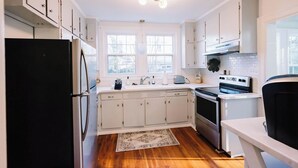 A kitchen with white cabinets, a black refrigerator, a stove, and a sink. - Beautiful Spacious 4 BR Retreat in Uptown with Fire Pit & Porch (Martinsville)