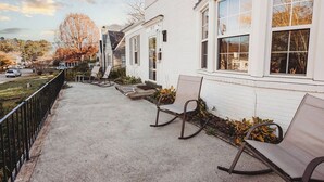 A white building with a number 217 on the door, a concrete pathway, and two rocking chairs. - Beautiful Spacious 4 BR Retreat in Uptown with Fire Pit & Porch (Martinsville)