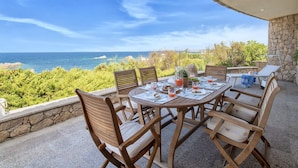 Une table ronde en bois, entourée de chaises, placée sur une terrasse donnant sur la mer.