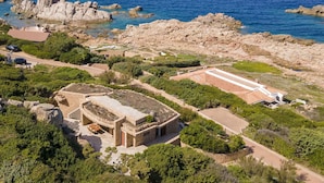 Une propriété située sur la côte, comprenant un grand bâtiment, un espace patio et une vue sur la mer.