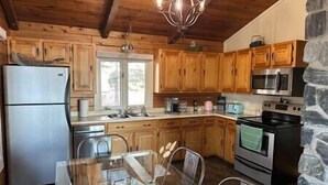 Eine Küche mit Holzausstattung, einem Edelstahl-Kühlschrank, einer Mikrowelle, einem Backofen und einem Glastisch mit Stühlen.