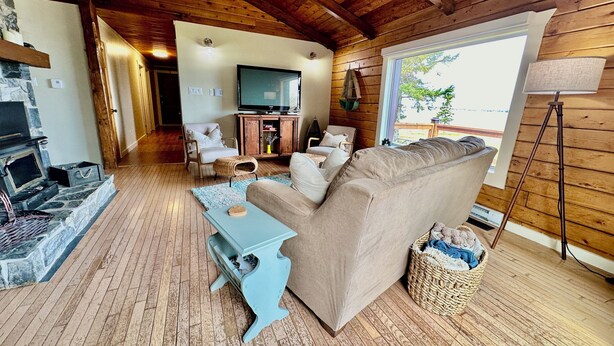 Ein gemütliches Blockhaus-Interieur mit Kamin aus Stein, Holzdielen, einem großen Sofa und einem Fernseher.