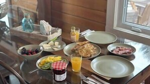 Ein Esstisch mit verschiedenen Speisen, darunter Obst, Käse und Fleisch, sowie ein Glas Orangensaft.