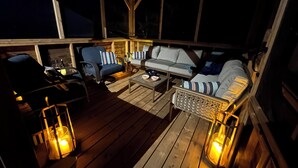 Eine Holzterrasse mit einer Couch, Stühlen und einem Tisch, beleuchtet von Laternen.
