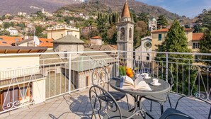 Un balcon avec une table et des chaises, donnant sur une ville avec ses bâtiments et le clocher d’une église.