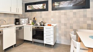 Une cuisine moderne avec des meubles blancs, un four encastré, une machine à café et une fenêtre au-dessus de l’évier.