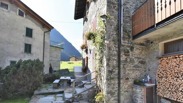 A stone building with a staircase leading to a wooden deck, surrounded by greenery and a mountain view. - Nice apartment for 4 people with WIFI, TV and pets allowed (Tartano)