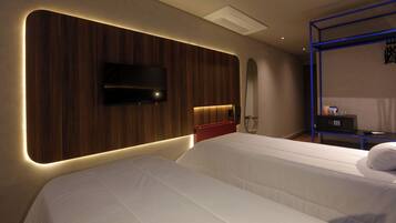 Ein Hotelzimmer mit zwei Betten, einem an einer Holzpaneele befestigten Fernseher, einem kleinen Schreibtisch mit einer Mikrowelle und einem Fahrrad in der Ecke.