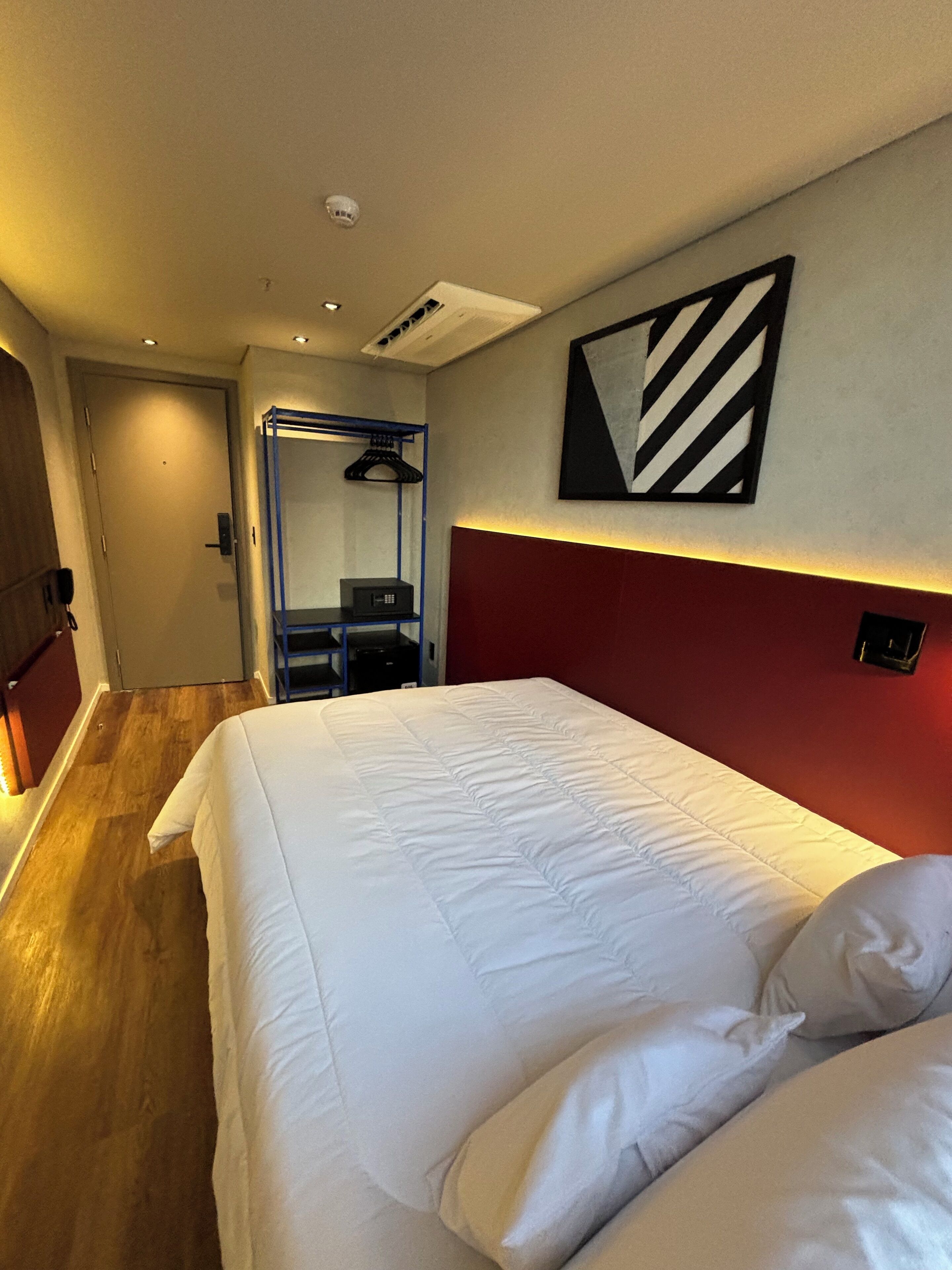 Una camera d'albergo con un letto rifatto, una parete decorata in rosso e un quadro astratto moderno.