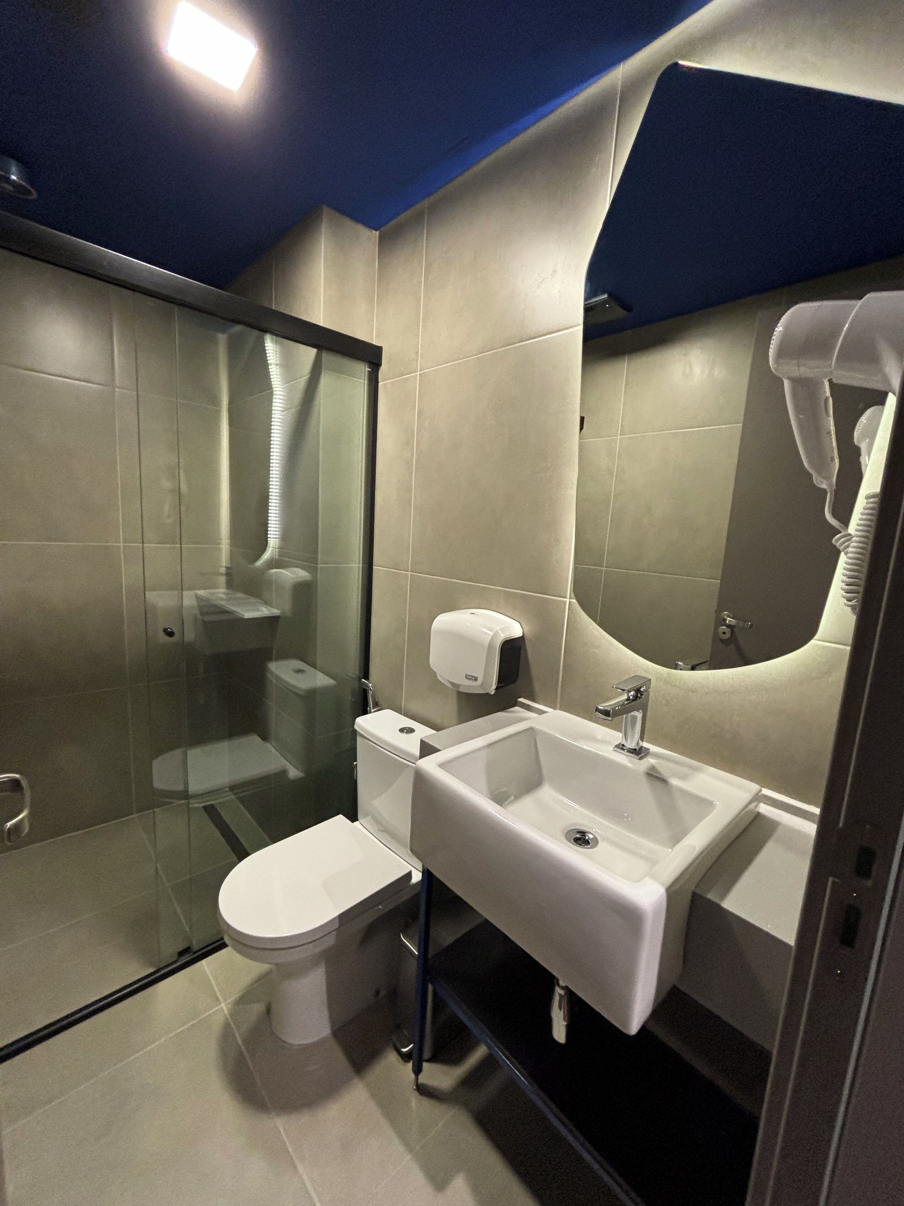 Une salle de bain moderne avec une douche à parois de verre, des toilettes, un lavabo avec un miroir et un sèche-cheveux fixé au mur.