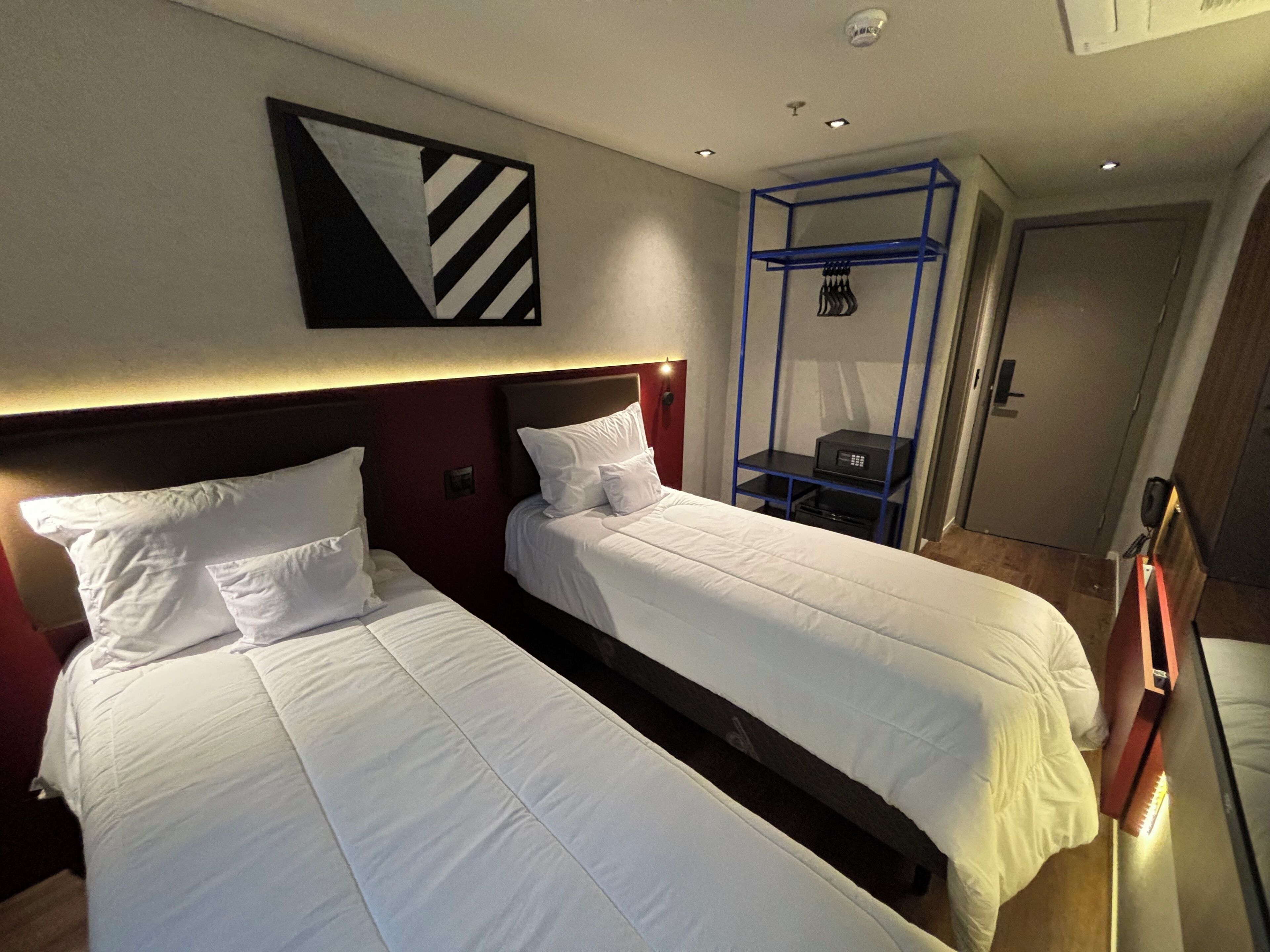Een hotelkamer met twee bedden, een blauwe plank en een kunstwerk aan de muur.