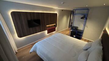 A modern hotel room with a large bed, a mounted TV, and a built-in wardrobe.