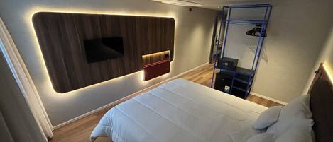 Una habitación de hotel moderna con una cama grande, un televisor montado y un armario empotrado.