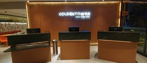 A hotel reception area with a modern design, featuring a reception desk, two computer stations, and a large illuminated sign displaying the hotel name.