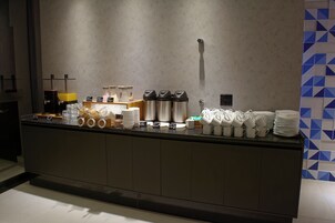Buffet com diversas opções de comida e bebida, incluindo máquinas de café e uma seleção de pratos e copos.