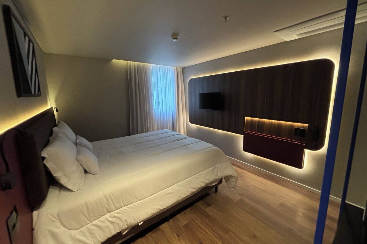 Une chambre d’hôtel moderne avec un grand lit, un téléviseur fixé au mur et un plancher en bois.