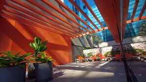 An outdoor seating area with potted plants, orange chairs, and a modern architectural design with reflective glass and orange structural elements. - Golden Tower Express Nações Unidas by Fênix Hotéis (São Paulo)
