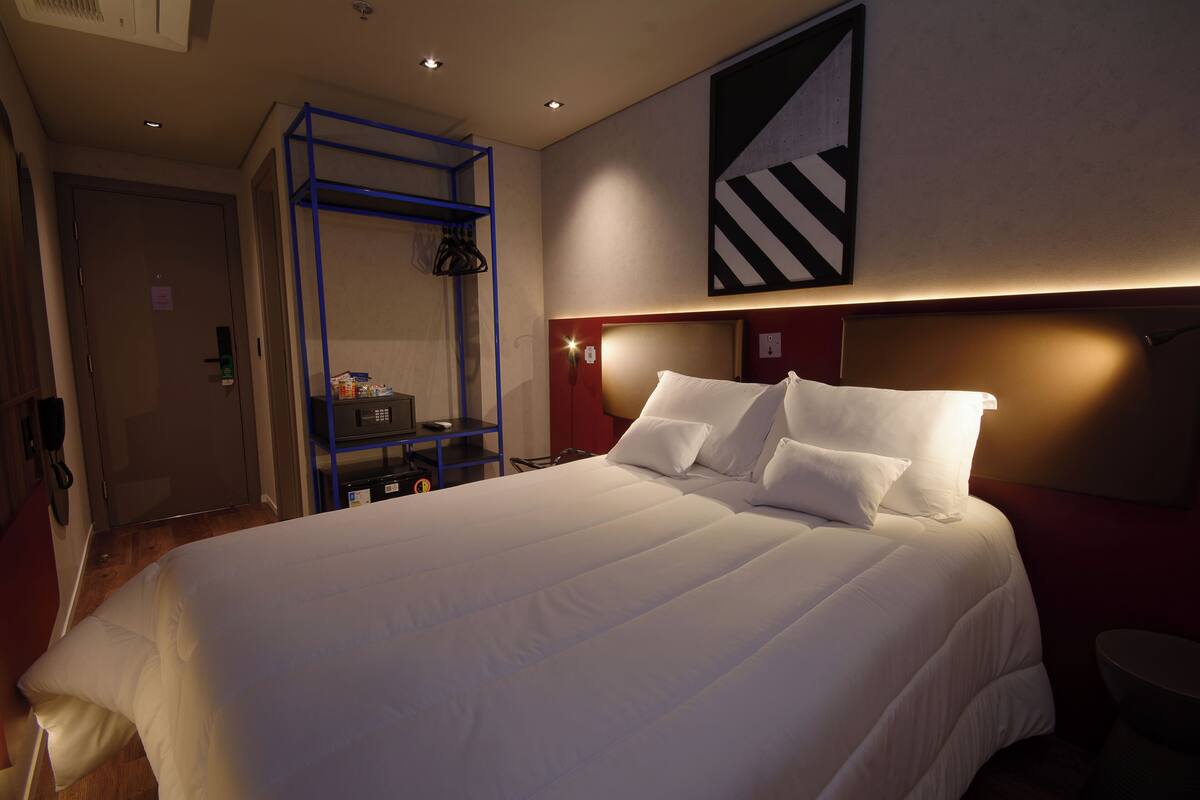 Une chambre d’hôtel avec un grand lit, une étagère bleue et une œuvre d’art moderne accrochée au mur.