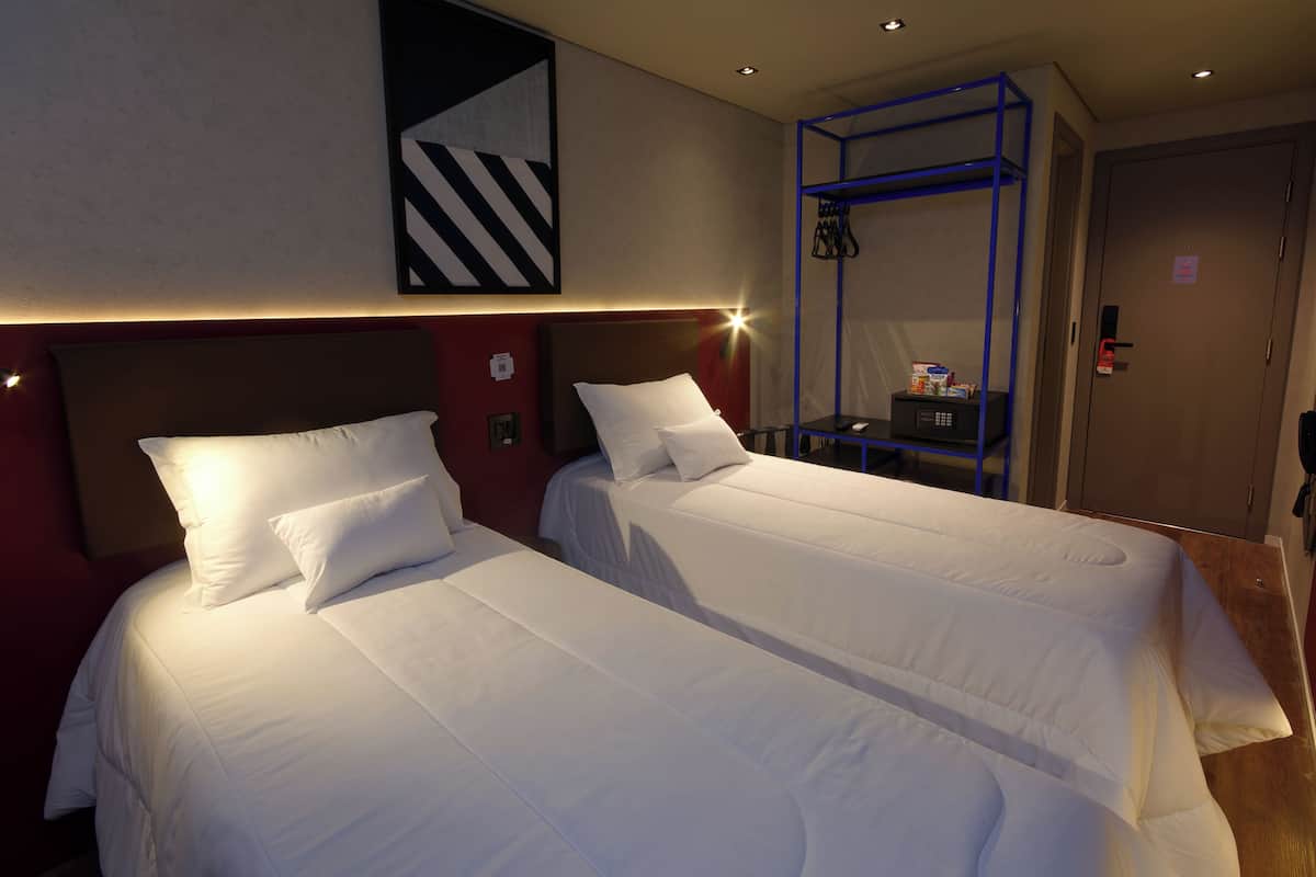 Une chambre d’hôtel avec deux lits, une étagère en métal bleue et une œuvre d’art accrochée au mur.