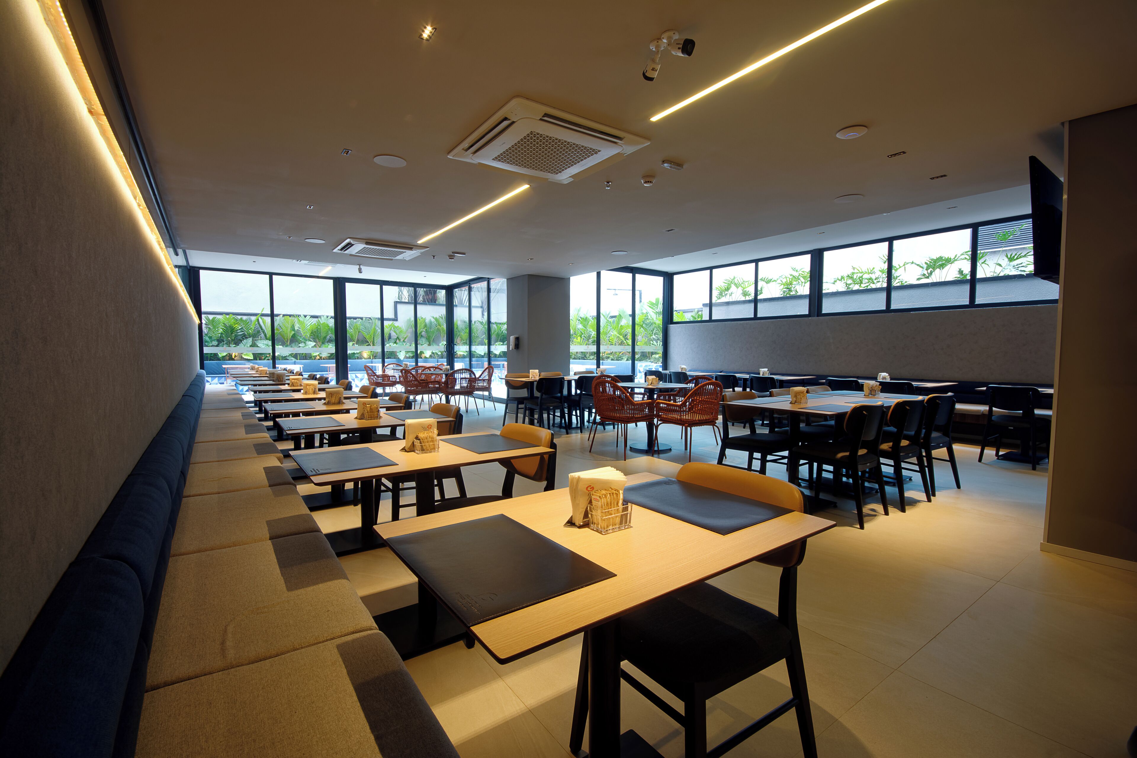 A spacious indoor area with multiple tables and chairs, large windows allowing natural light, and a modern ceiling design.