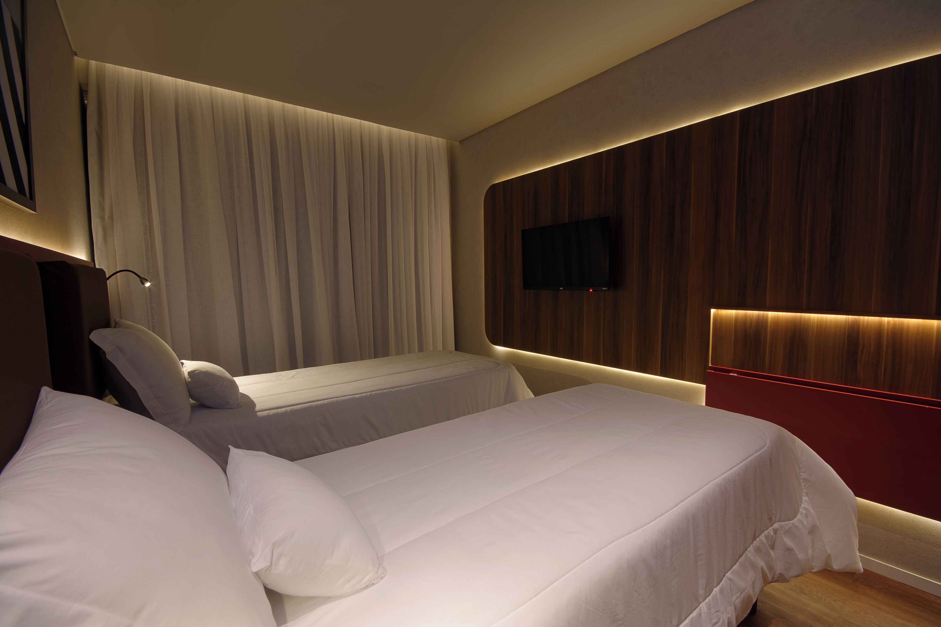 Een hotelkamer met twee bedden, een wandtelevisie en een groot raam met gordijnen.