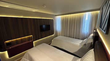 A hotel room with two beds, a TV mounted on the wall, and a window with curtains.
