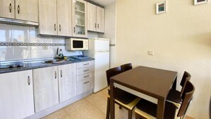 A compact kitchen with a dining area, featuring light-colored cabinets, a microwave, and a refrigerator. - Apartamento Miramar Calpe (Calpe)