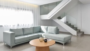 A modern living room with a light grey sectional sofa, a round wooden coffee table, and a glass staircase.