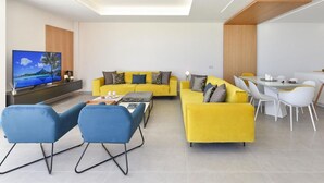 A modern living room with a yellow sofa set, a flat-screen TV, and a dining area with white chairs and a table.