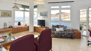 A modern living room with a large window overlooking the sea, a sofa, a TV, and a dining area with a table and chairs. - Nice apartment for 4 guests with WIFI, TV, terrace and pets allowed (Las Palmas De Gran Canaria)