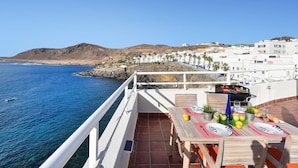 A terrace with a table set for dining, overlooking a coastal town and the sea. - Nice apartment for 4 guests with WIFI, TV, terrace and pets allowed (Las Palmas De Gran Canaria)