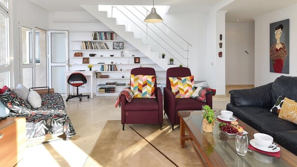 Un salon moderne comprenant un canapé, deux fauteuils, une table basse et un escalier menant à une mezzanine.