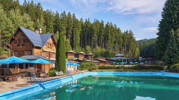 Eine Holzlodge mit Schwimmbecken, umgeben von hohen Bäumen.