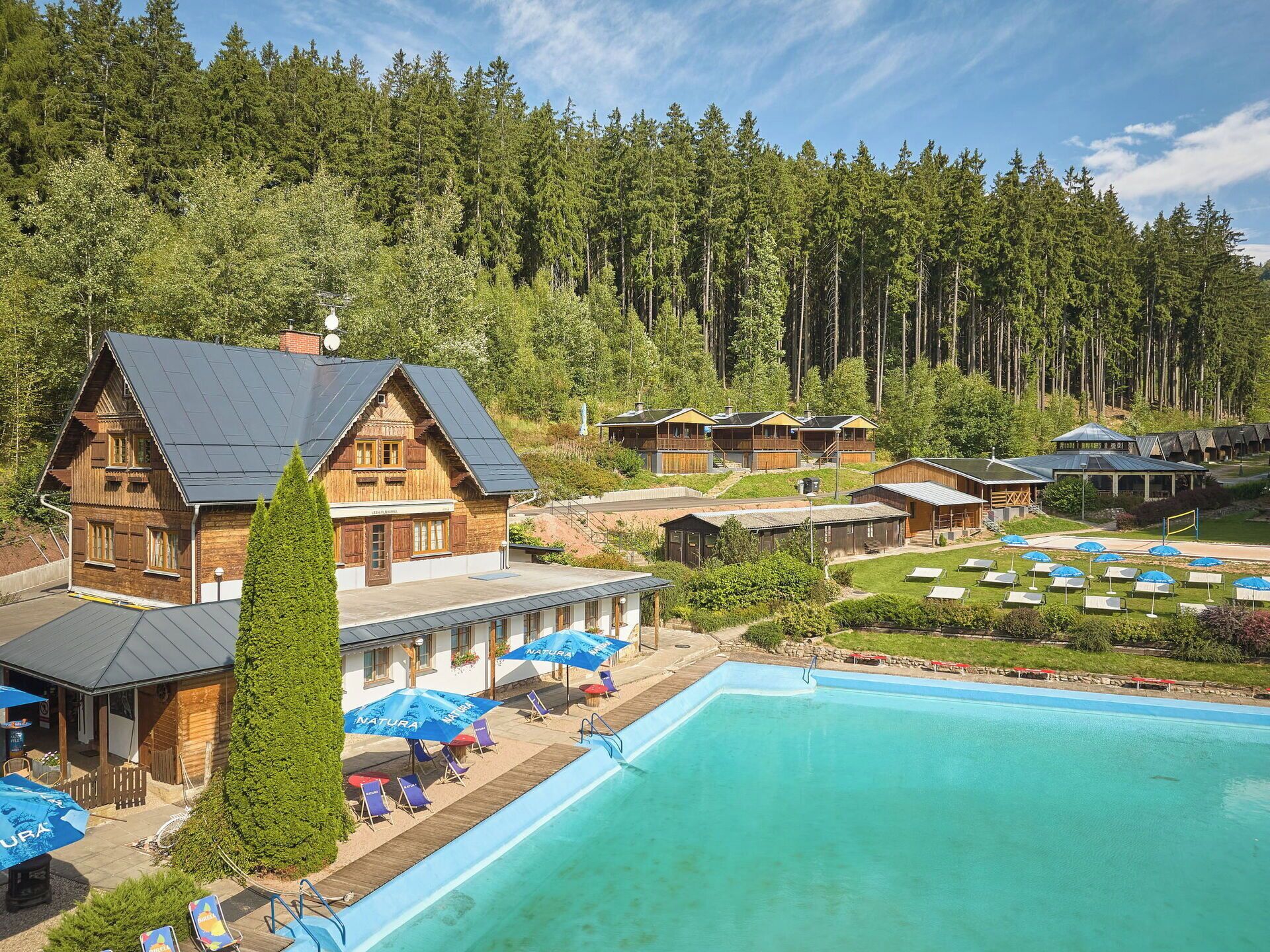 Een resort met een zwembad, houten huisjes en een bebost achtergrond.