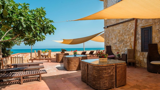 An outdoor seating area with wicker furniture, a storage box, and a view of the sea.